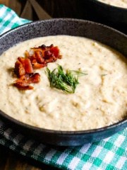 A bowl of cream of celery soup on a checkered napkin on the table.