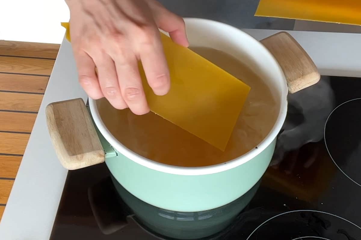 Adding the lasagna noodles to the pot to cook.