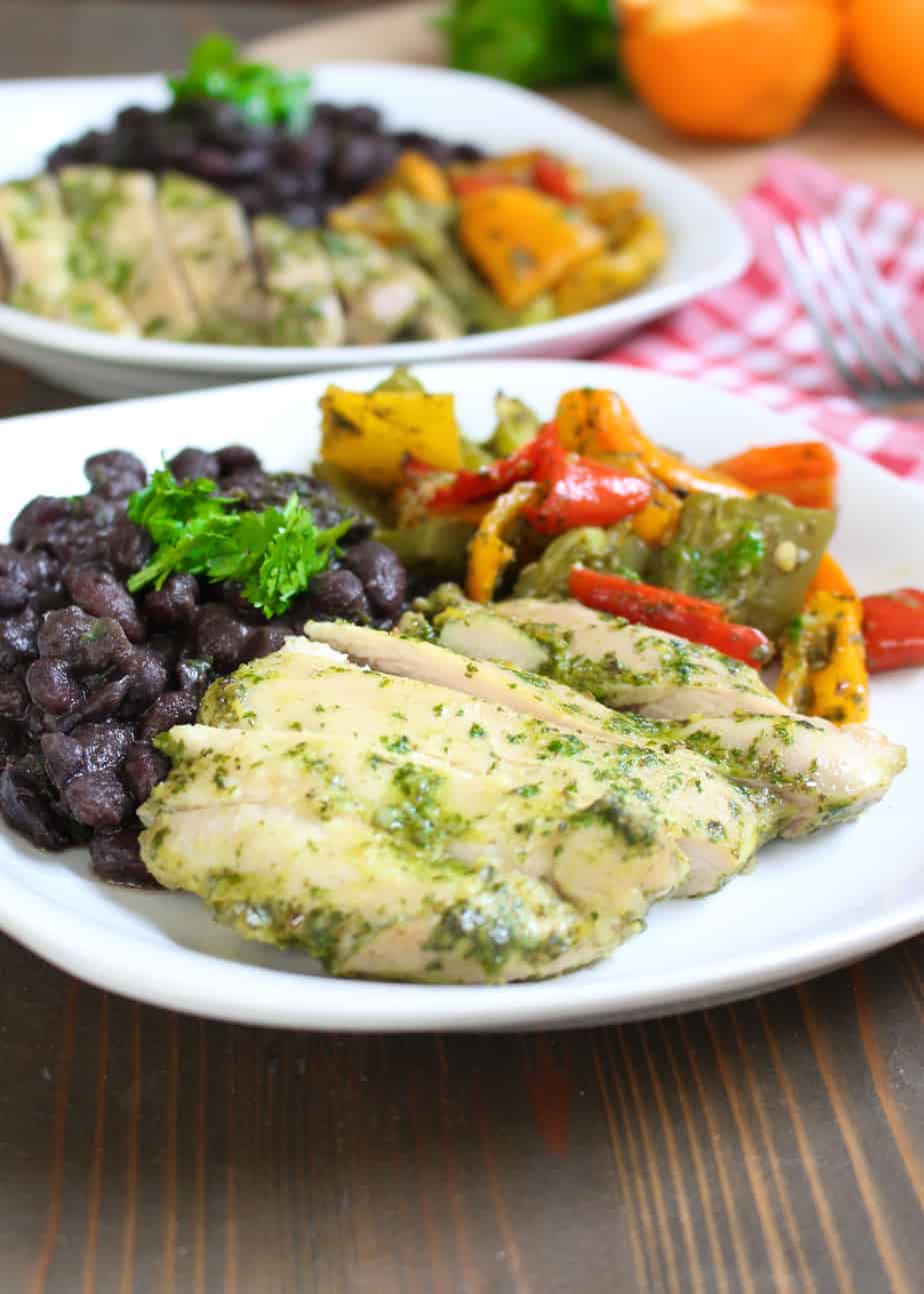 cilantro orange chicken on a white plate with black beans and roasted peppers