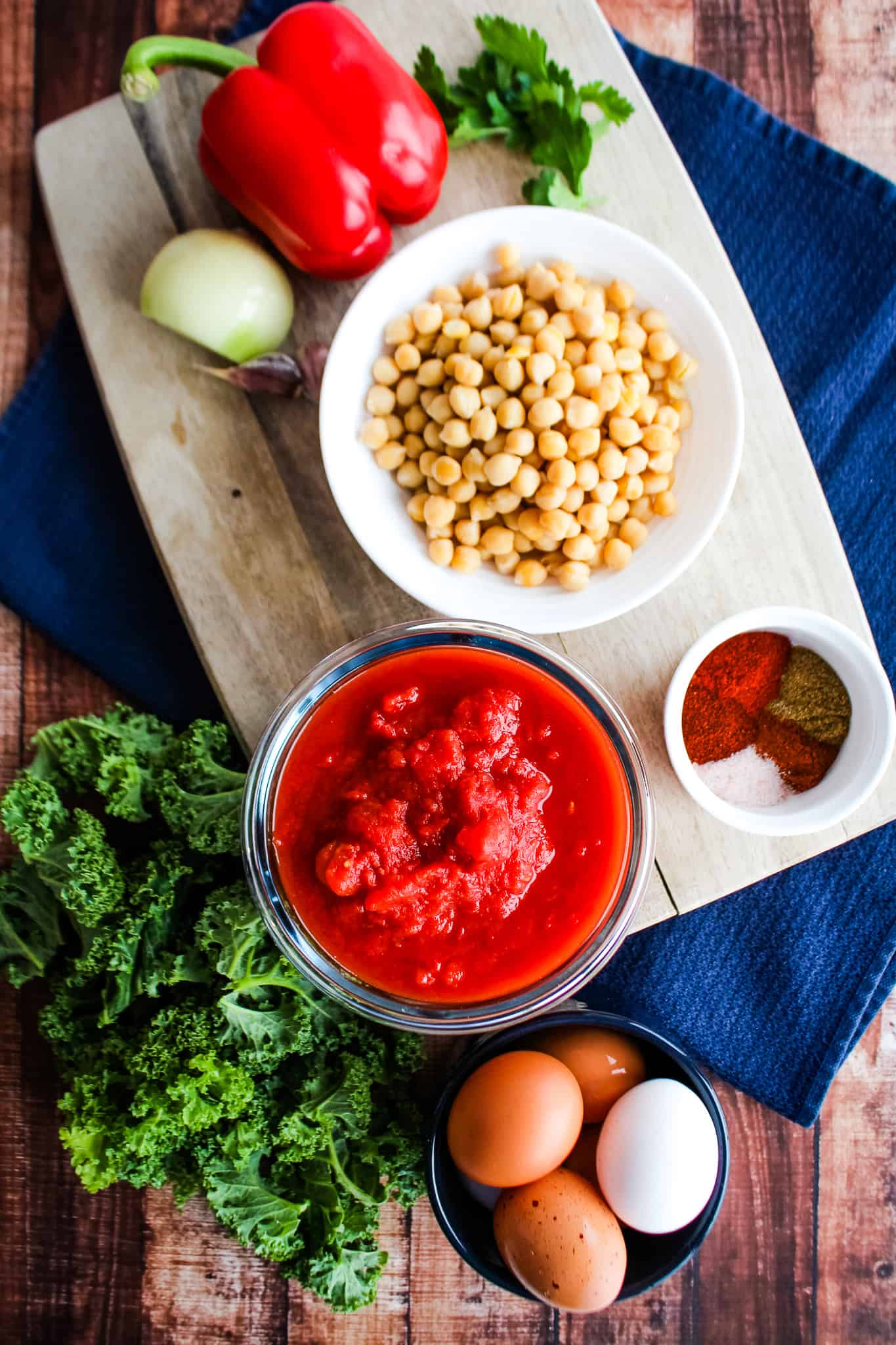 Ingredients displayed: bell pepper, white onion, chickpeas, canned tomatoes, spices, kale, eggs. 