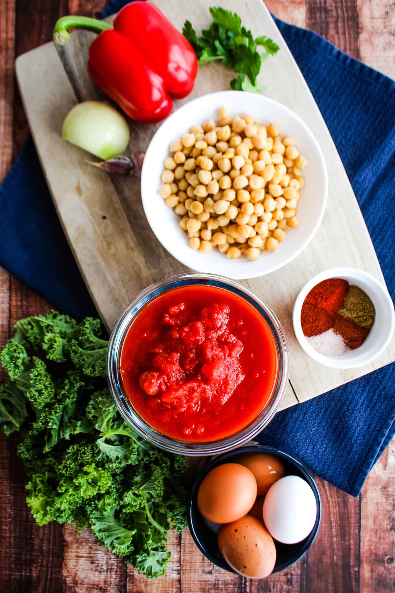 Ingredients displayed: bell pepper, white onion, chickpeas, canned tomatoes, spices, kale, eggs.