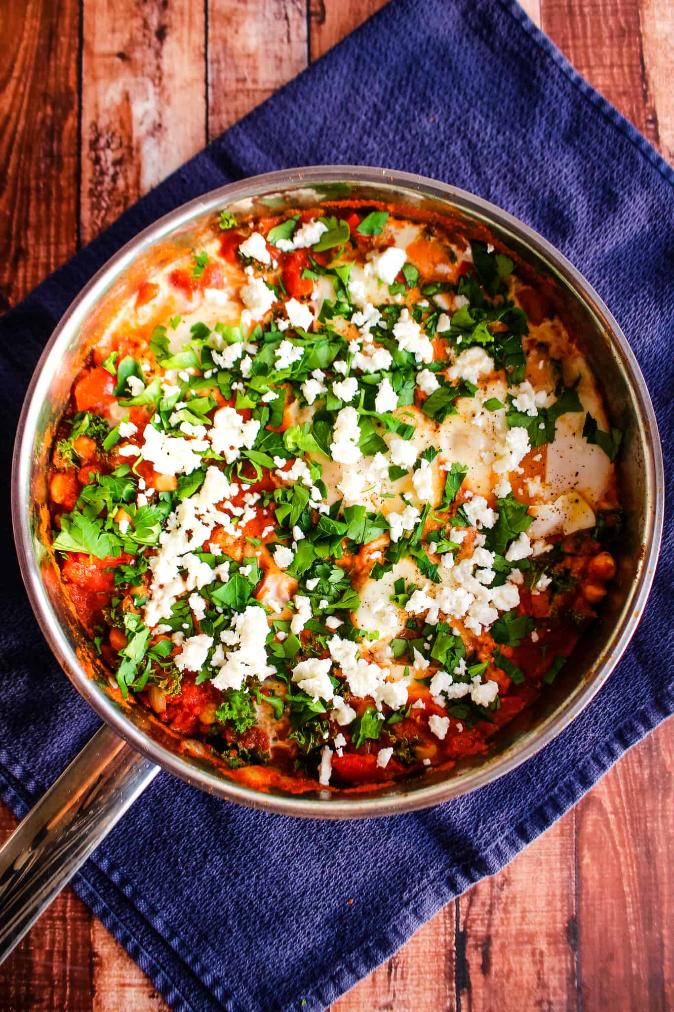 Shakshuka in a skillet topped with parsley and feta, on a blue napkin.