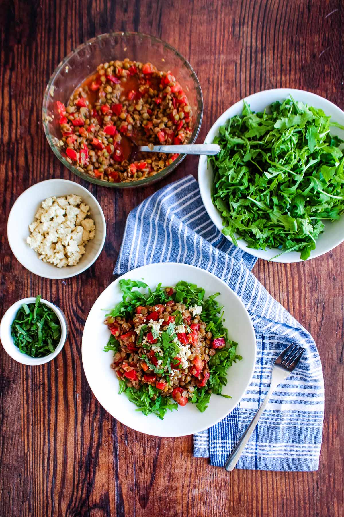 Lentil salad on the table with bowls of feta, lentil bruschetta, feta cheese, and basil on the table.