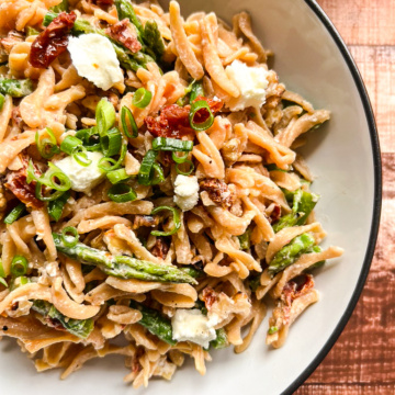 Large bowl with completed pasta salad of asparagus, goat cheese, sun dried tomatoes, walnuts, and topped with green onion.