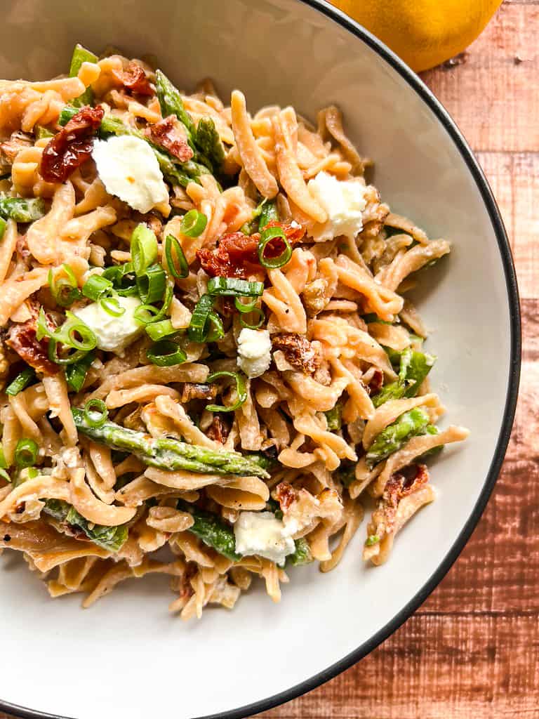 Large bowl with completed pasta salad of asparagus, goat cheese, sun dried tomatoes, walnuts, and topped with green onion.