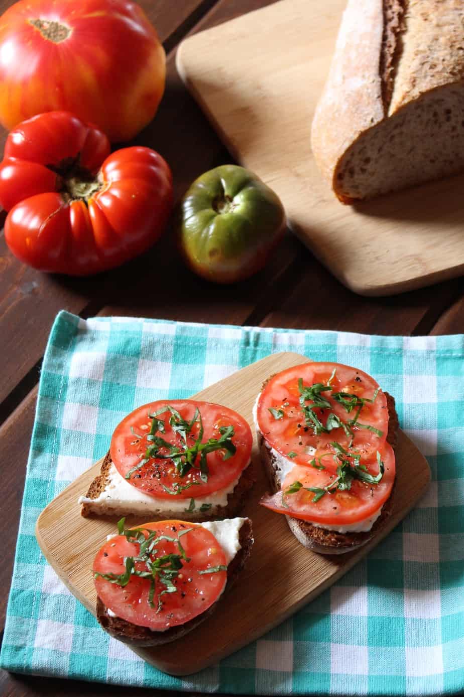 tomatoes and bread beside three slices of garlic ricotta toast, topped with tomato slices, basil, and seasonings