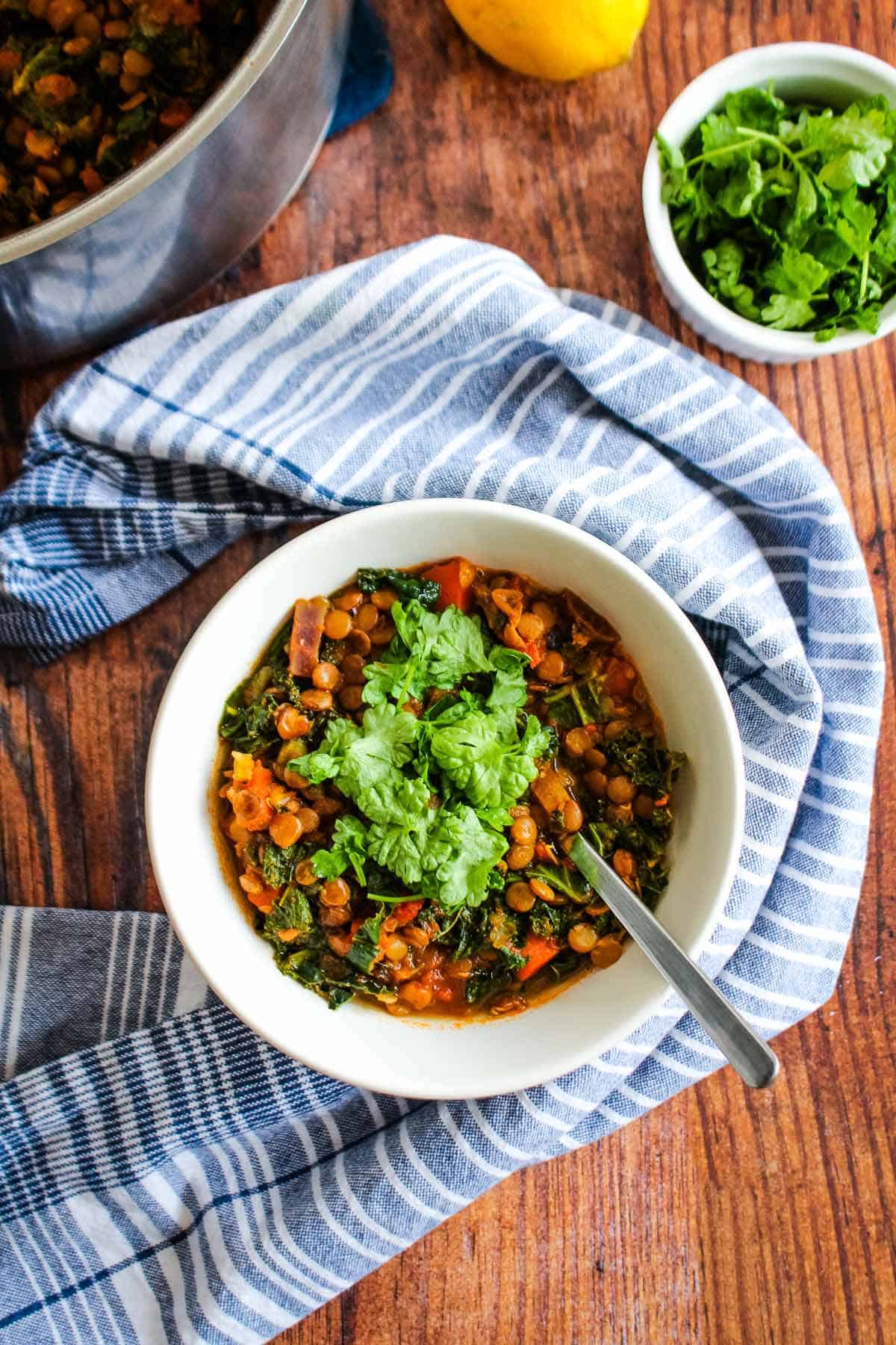 A bowl of lemon lentil and kale soup on the table with a spoon in the bowl.