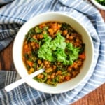 A bowl of lentil kale soup flavored with lemon on the table.