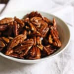 Bowl spicy candied pecans on a linen napkin on the table.