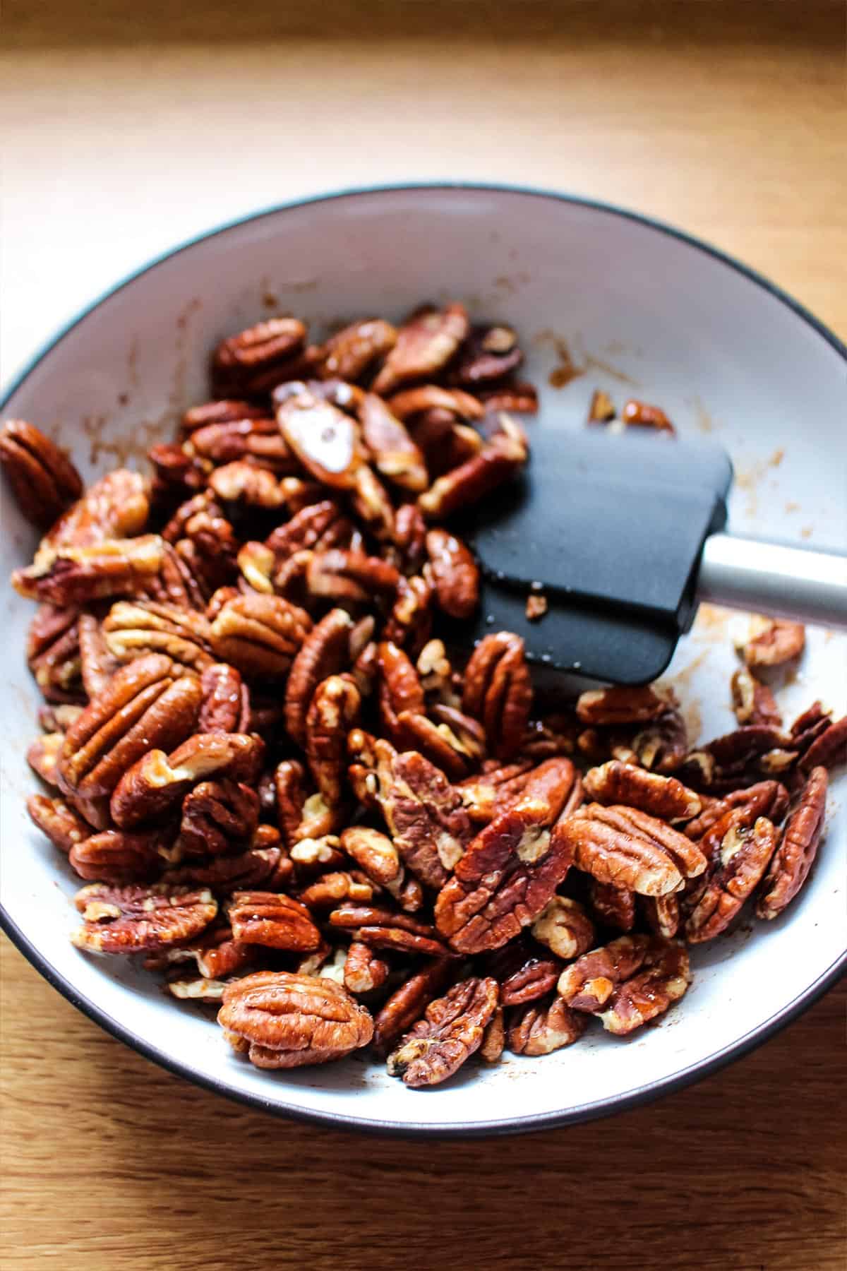 Nuts in a bowl moved around with spatula to coat with sweet and spicy flavors.