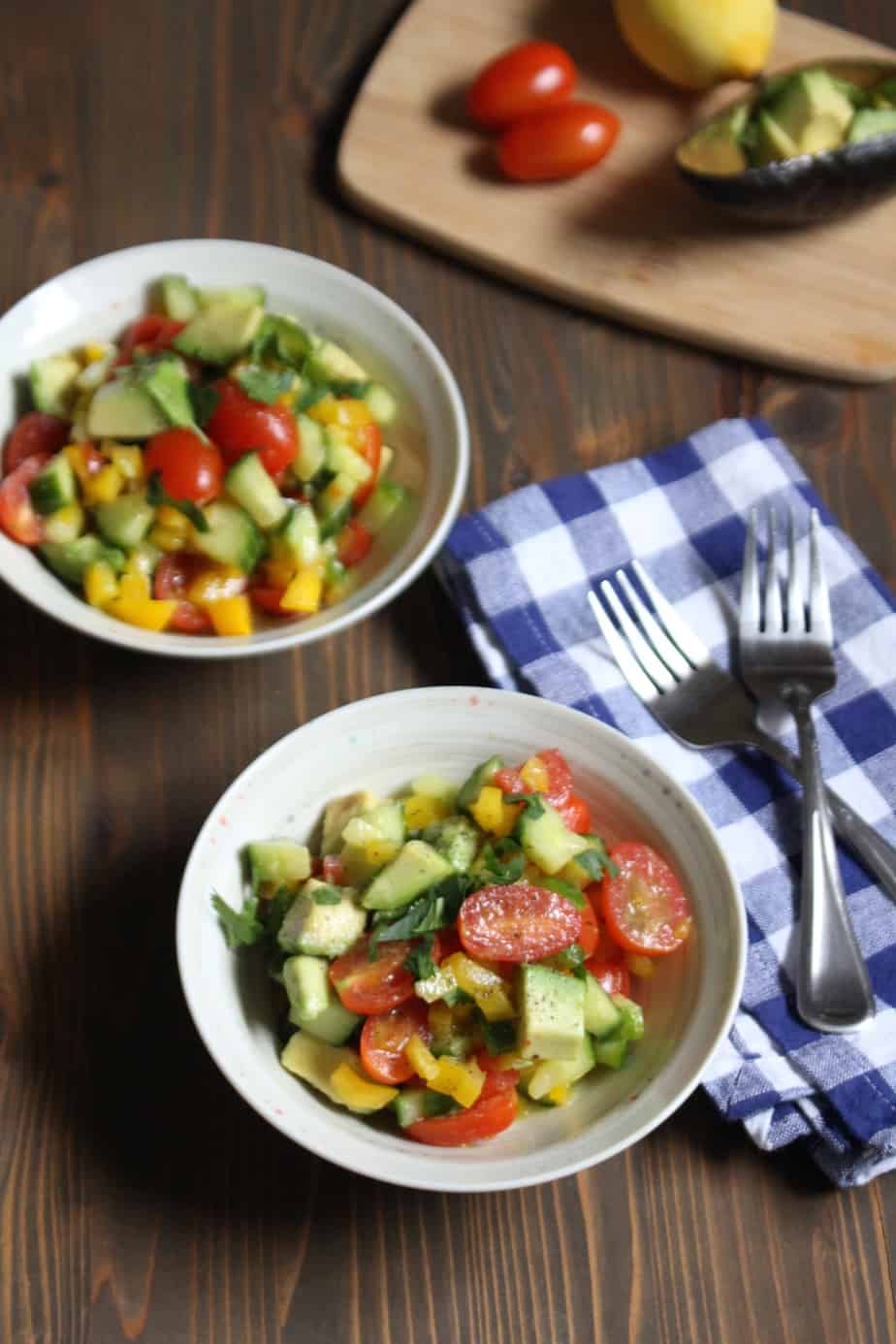 two bowls of easy summer vegetable salad made up of tomato, cucumber, avocado, and bell pepper