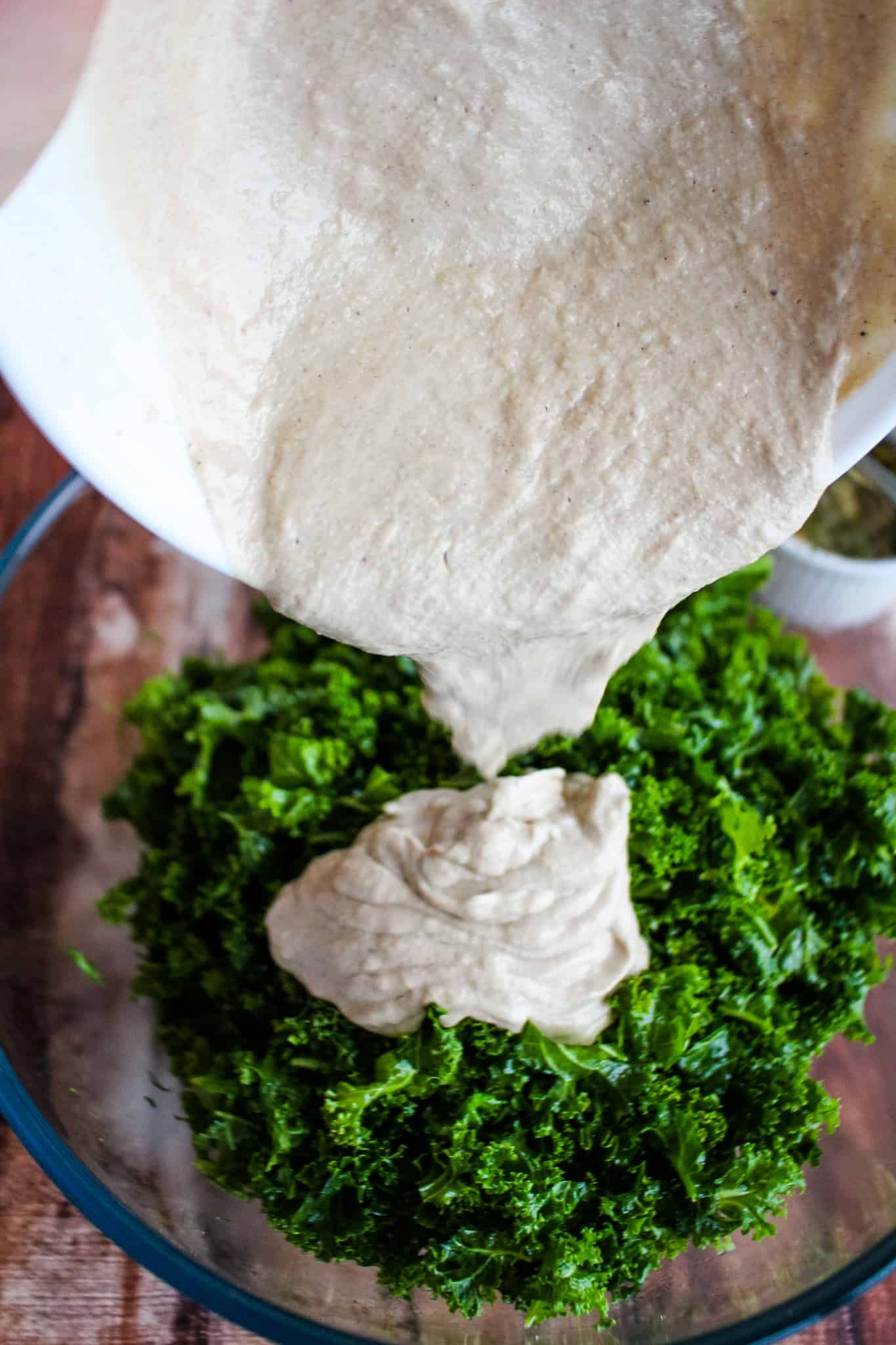 pouring thick tahini dressing over kale.