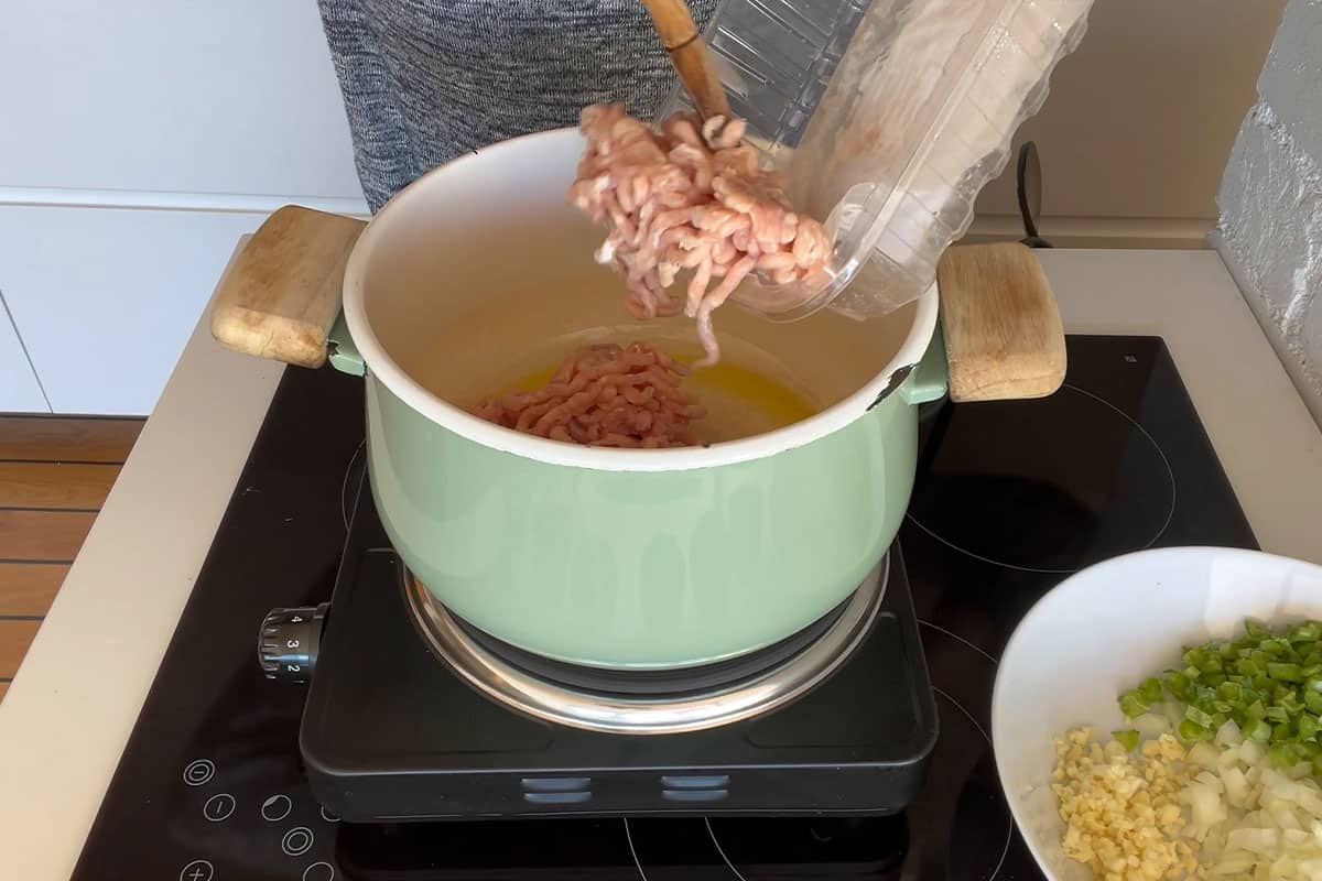 Adding ground turkey to the pot to cook.