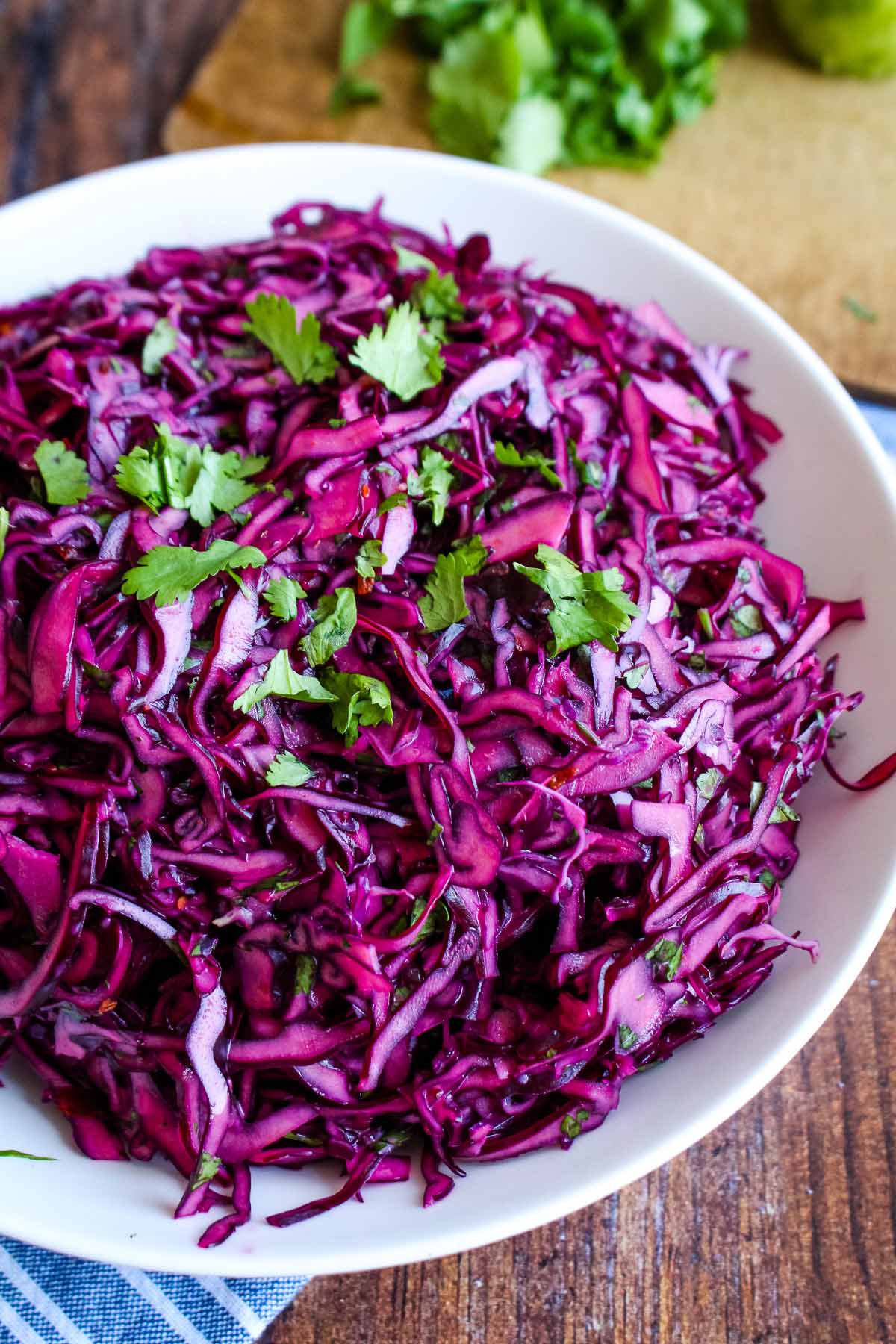 A half bowl of red cabbage slaw on the table garnished with fresh cilantro.