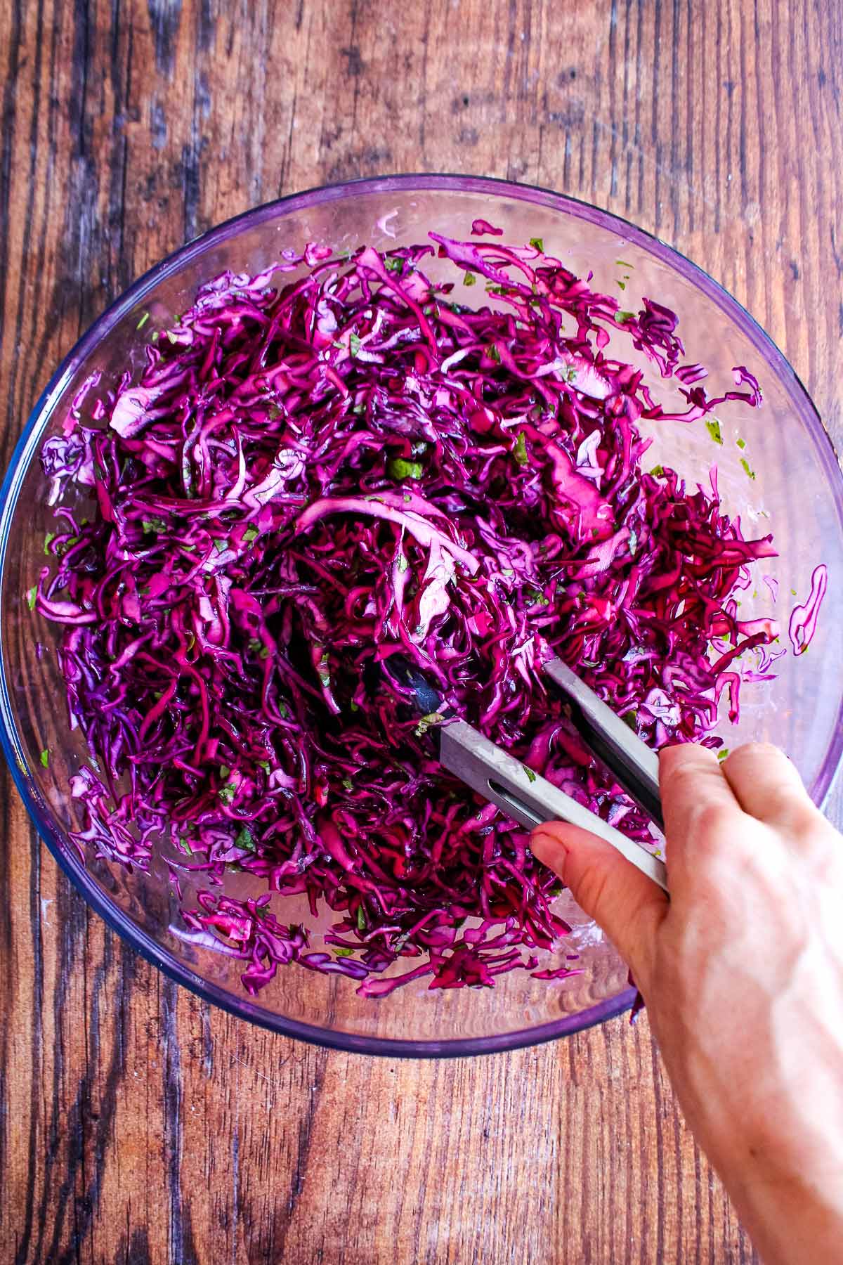 Mixing up the red cabbage slaw with tongs in a bowl.