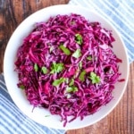 A bowl of red cabbage slaw on the table with cilantro on top.