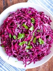 A bowl of red cabbage slaw on the table with cilantro on top.