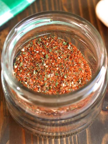 A jar of Italian sausage seasoning on the table with a small wooden spoon.