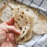 A hand holding up a folded cassava flour tortilla over the pan.