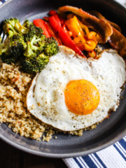 Close up bowl of quinoa, roasted broccoli, roasted bell peppers, and a fried egg.