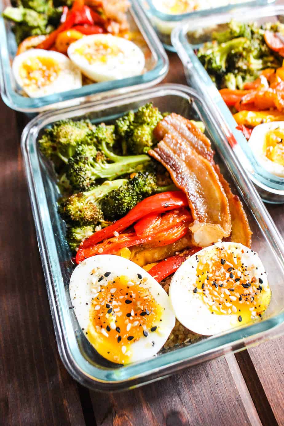 Glass container with roasted broccoli, bell peppers, bacon, and jammy eggs.