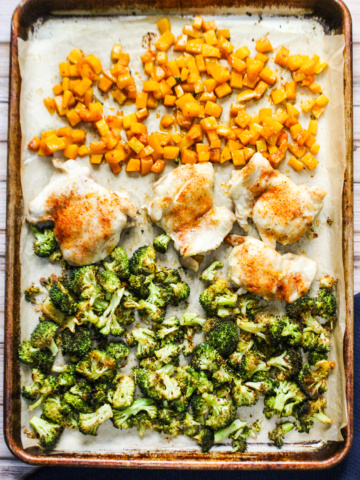 Sheet pan with cooked cubed butternut squash, four chicken thighs, and broccoli
