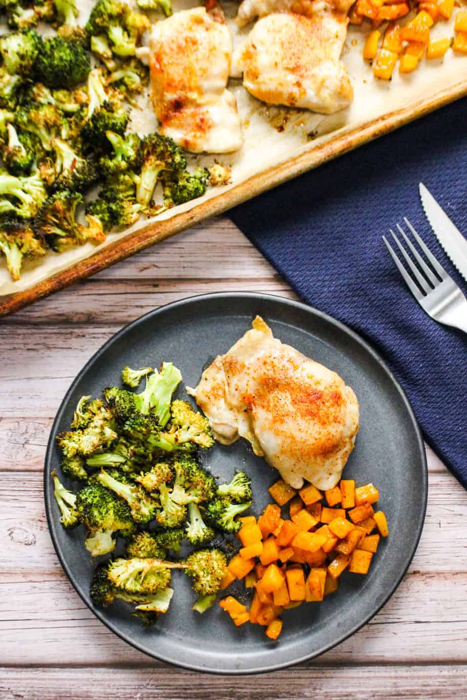 Juicy sheet pan chicken thigh on a plate beside roasted broccoli and butternut squash