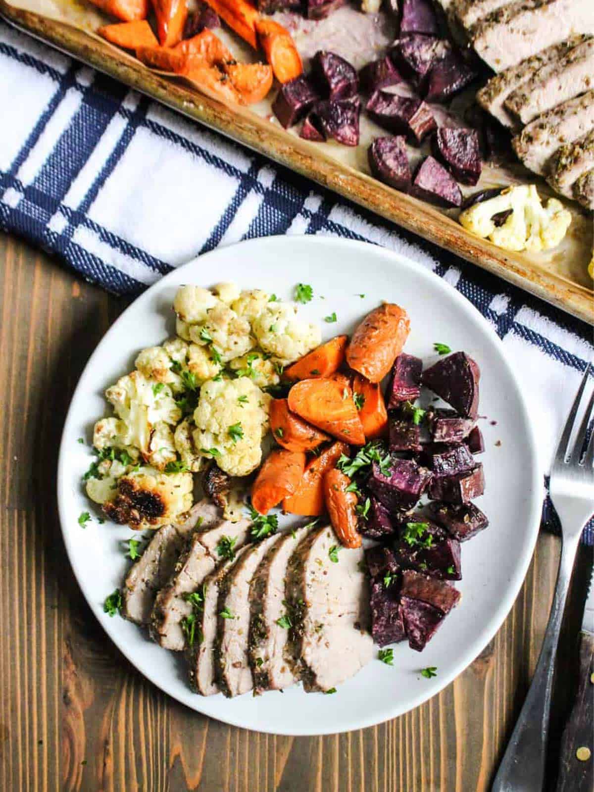 Plate with cooked pork, cauliflower, carrots, and purple sweet potatoes.