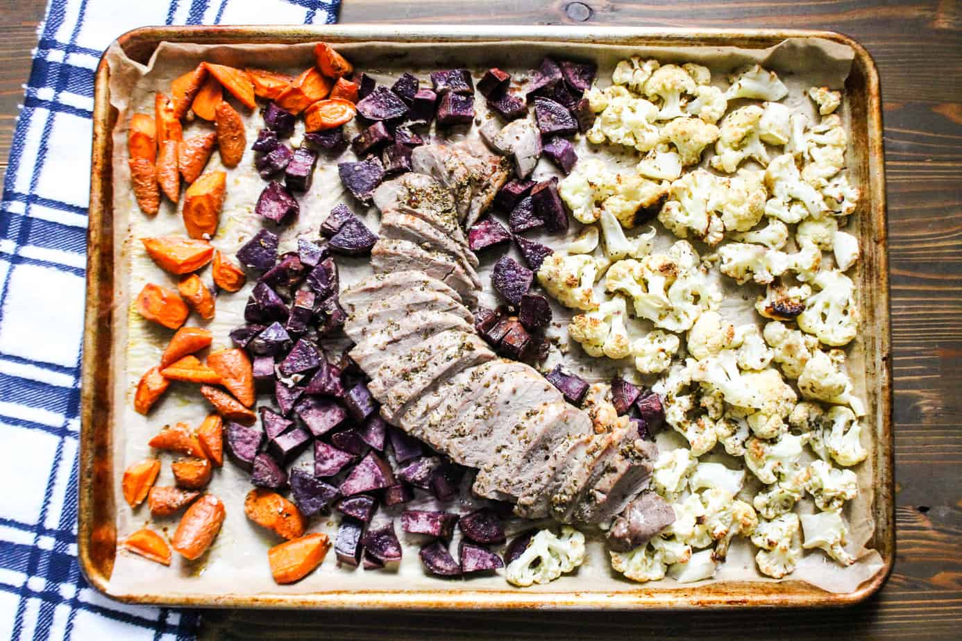 Sheet pan with cooked carrots, purple potatoes, cauliflower, and sliced pork tenderloin.