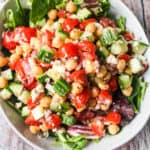 bowl of mixed greens with mediterranean chickpea salad, chickpeas, grape tomatoes, cucumbers, marinated red onions, feta