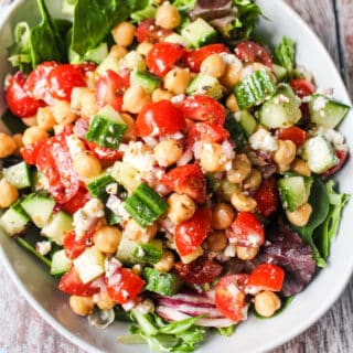 bowl of mixed greens with mediterranean chickpea salad, chickpeas, grape tomatoes, cucumbers, marinated red onions, feta