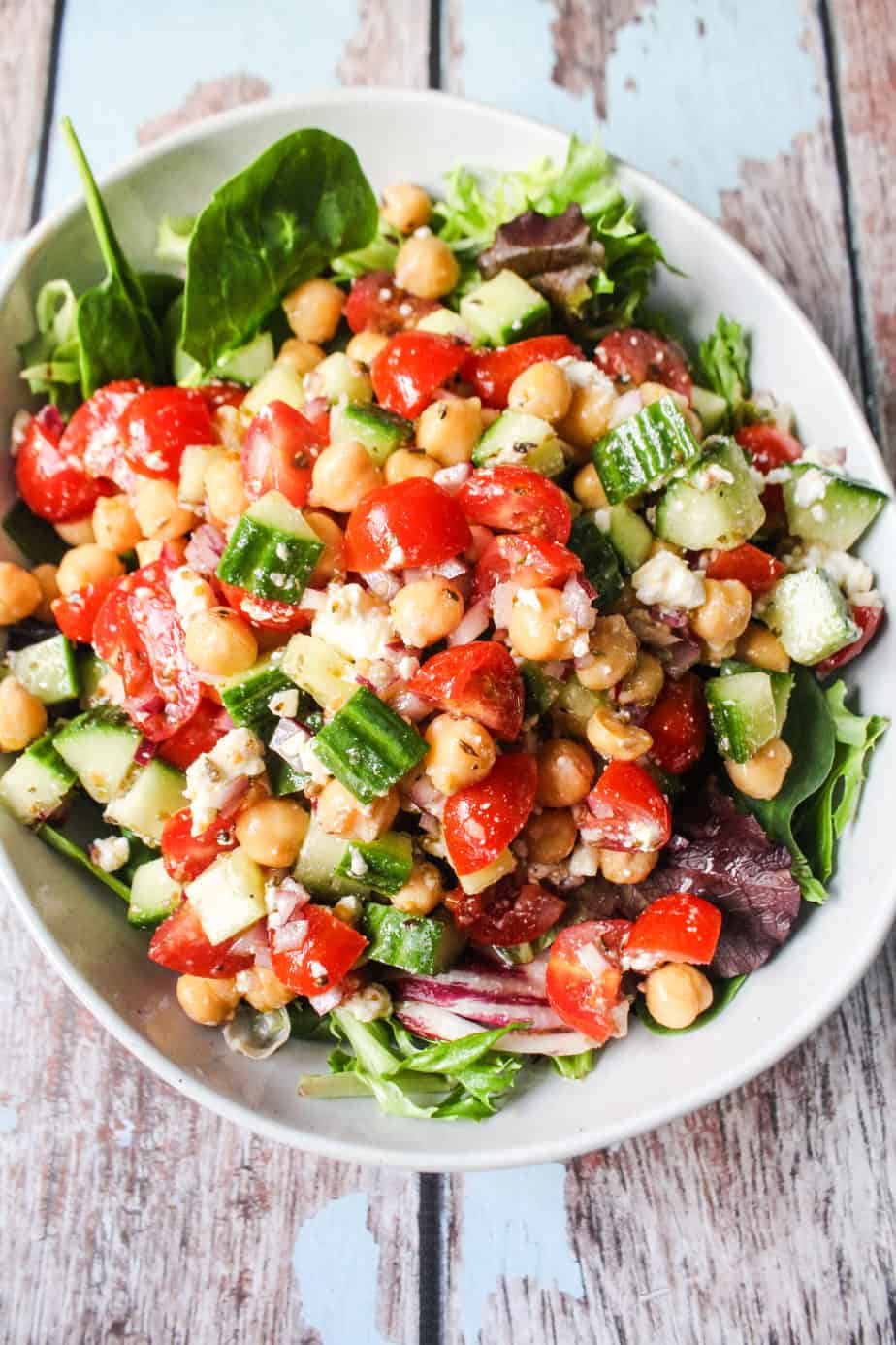 bowl of mixed greens with mediterranean chickpea salad, chickpeas, grape tomatoes, cucumbers, marinated red onions, feta