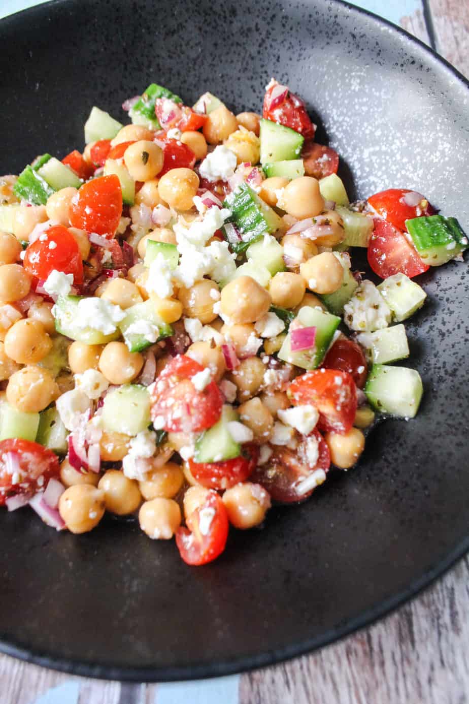 black bowl with chickpeas, cucumbers, grape tomatoes, red onions, feta