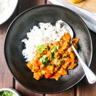 black bowl with white rice and butter chicken and vegetables