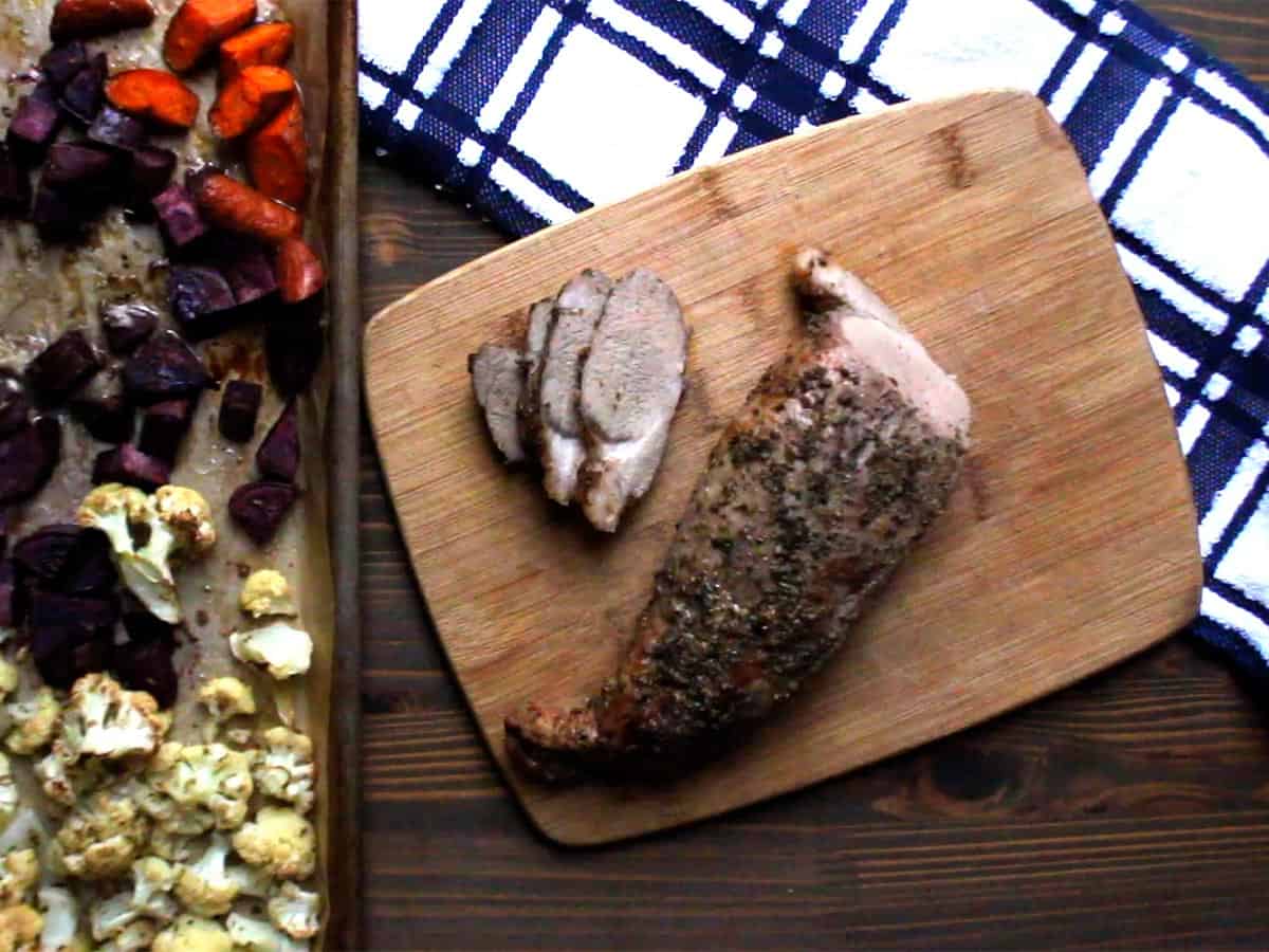 Cooked sheet pan pork tenderloin sliced on a cutting board.