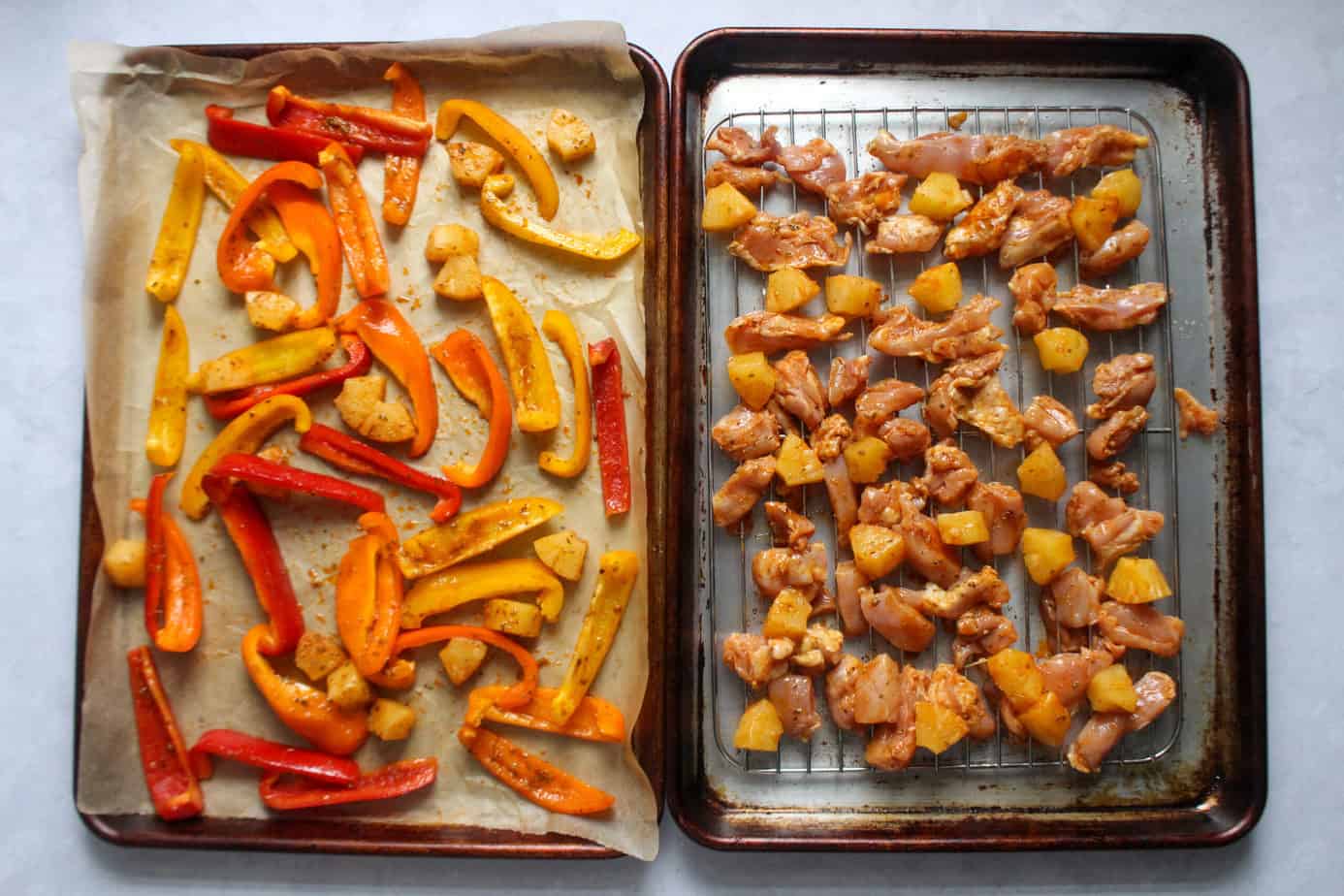 two sheet trays with sliced bell peppers, chicken, and pineapple