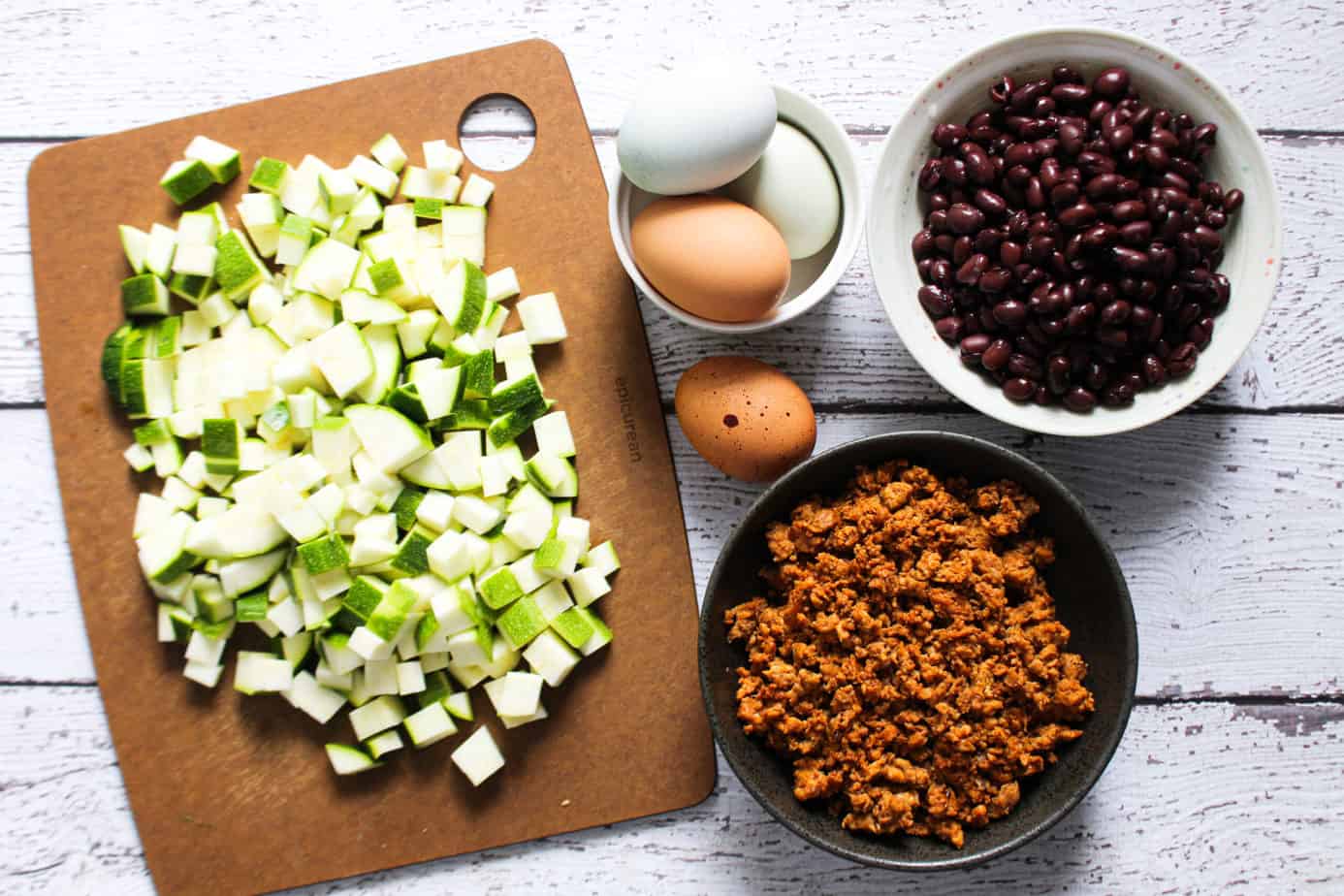 zucchini on a cutting board, raw whole eggs, chorizo, black beans