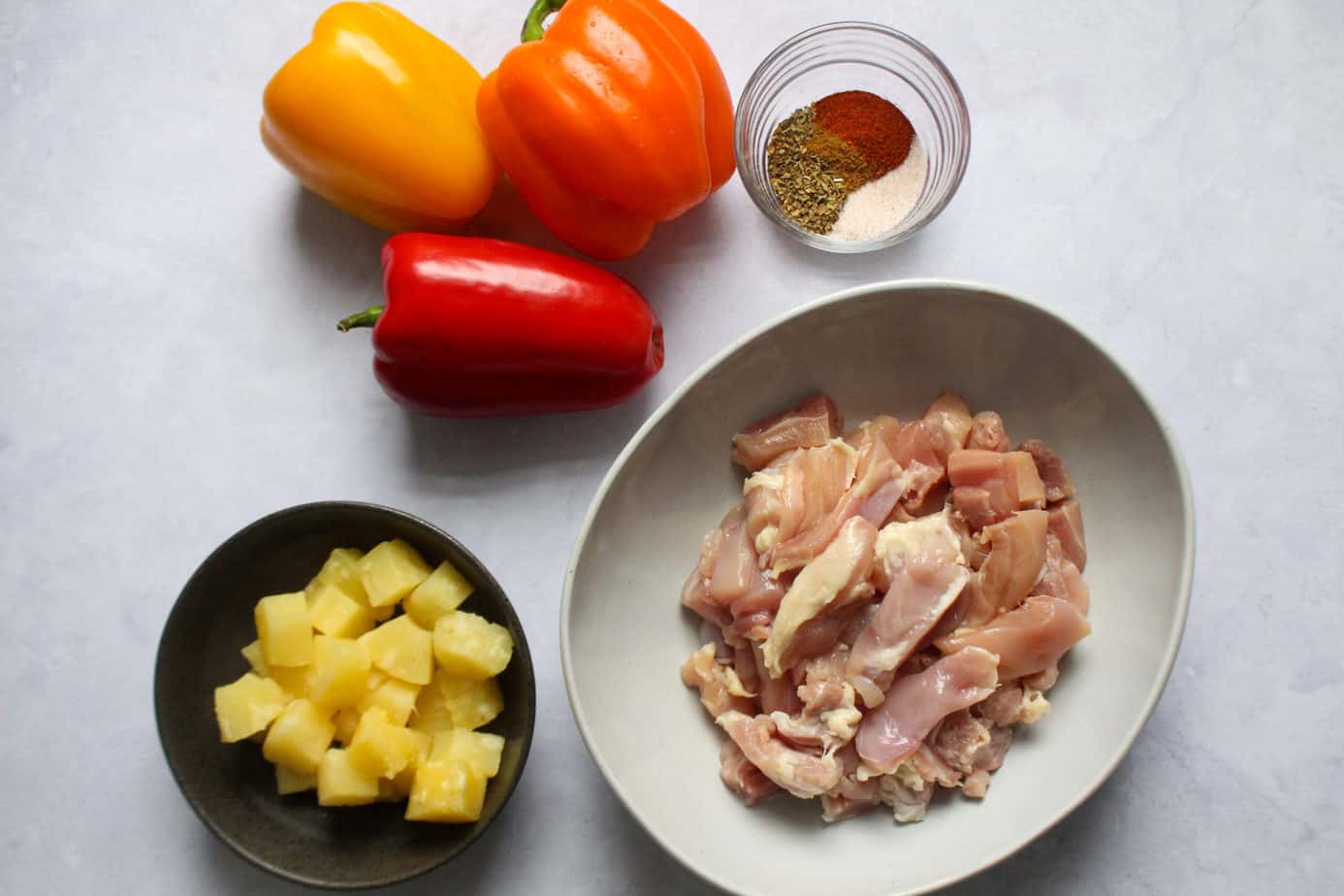 display of pineapple chunks, bell peppers, spices, and chopped raw chicken thighs