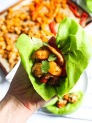 Hand holding a large leaf of butter lettuce filled with pineapple, bell peppers, and chicken.