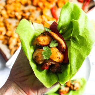 Hand holding a large leaf of butter lettuce filled with pineapple, bell peppers, and chicken.