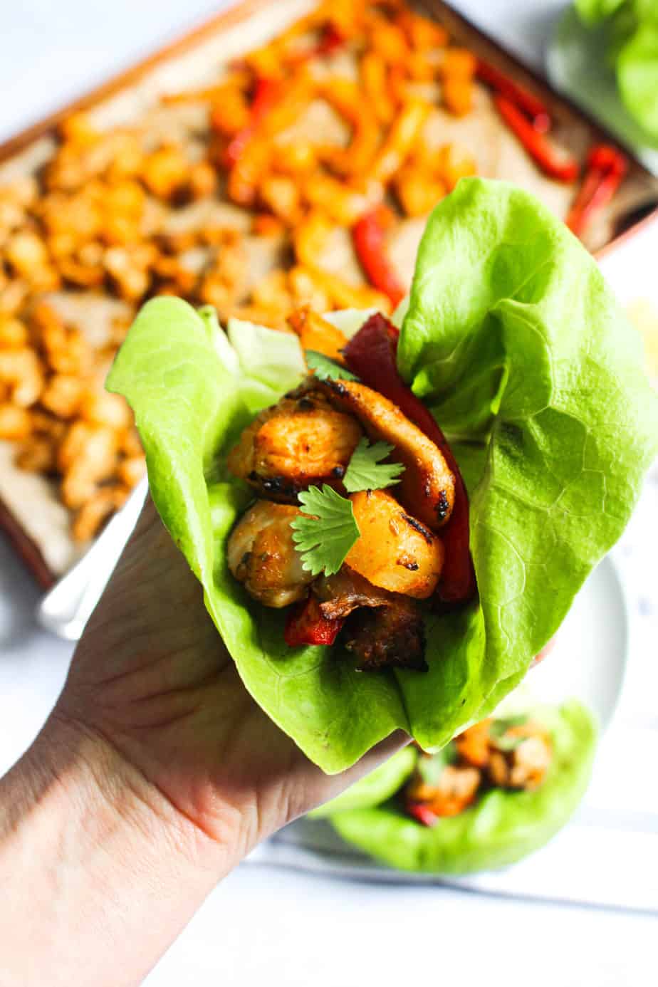 Hand holding a large leaf of butter lettuce filled with pineapple, bell peppers, and chicken.