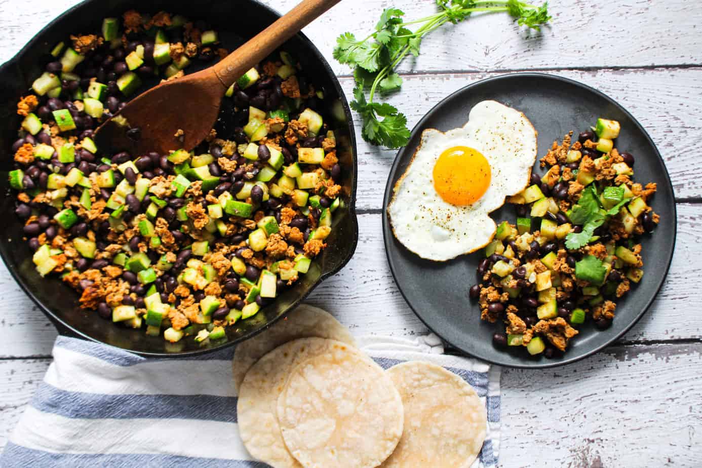 display of tortillas, cilantro, a plate with a sunny side up egg and a skillet with chorizo zucchini black beans