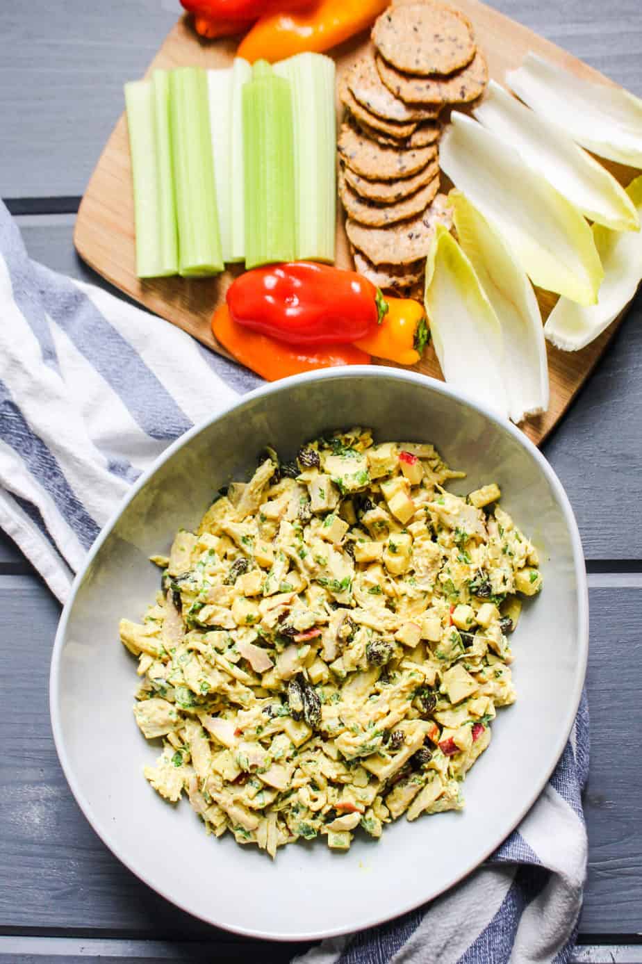 bowl of curry chicken salad next to a cutting board with crudité and crackers