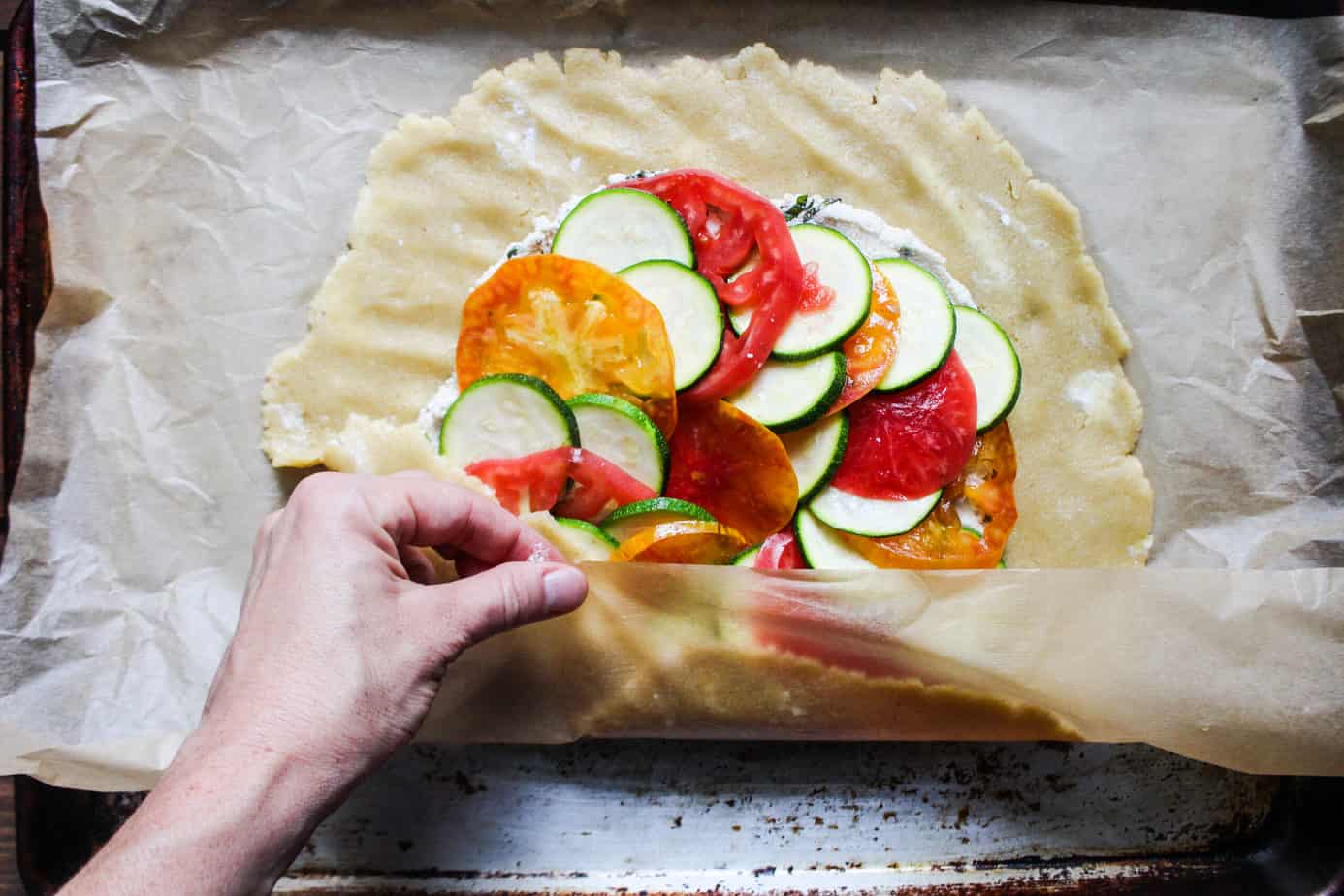 one hand using parchment paper to help fold the bottom of the galette over the vegetables