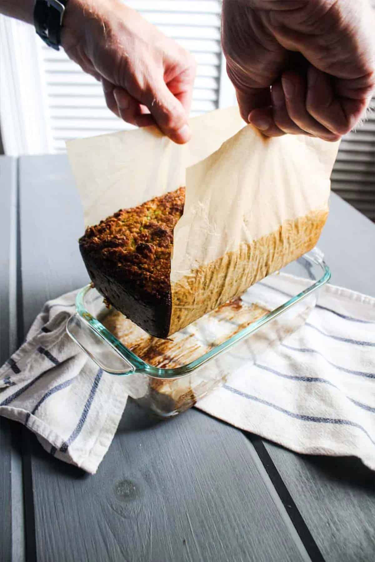 using parchment paper to remove Lifting cooked paleo zucchini bread from pan.