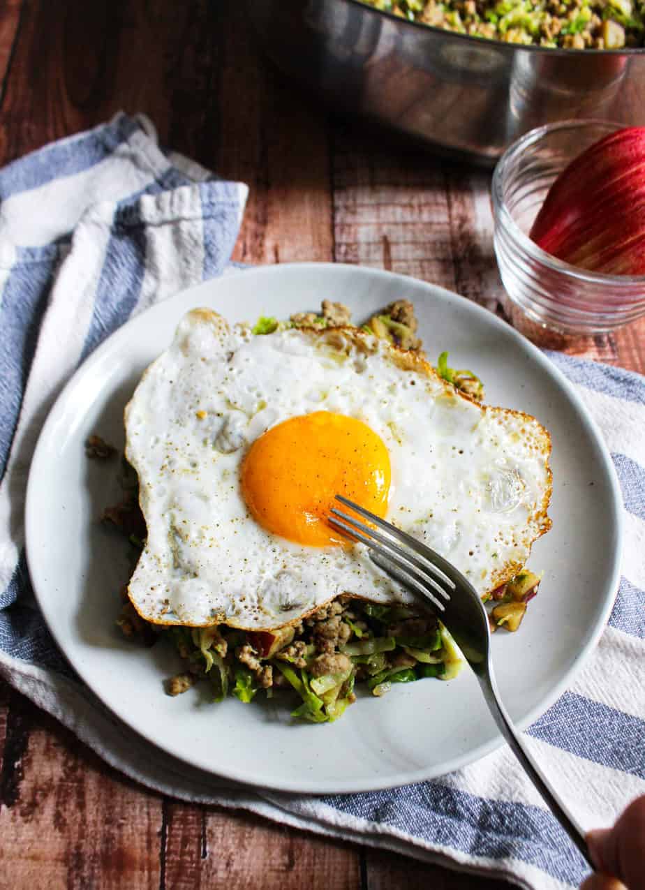 white plate with hash topped with sunny side up fried egg and fork