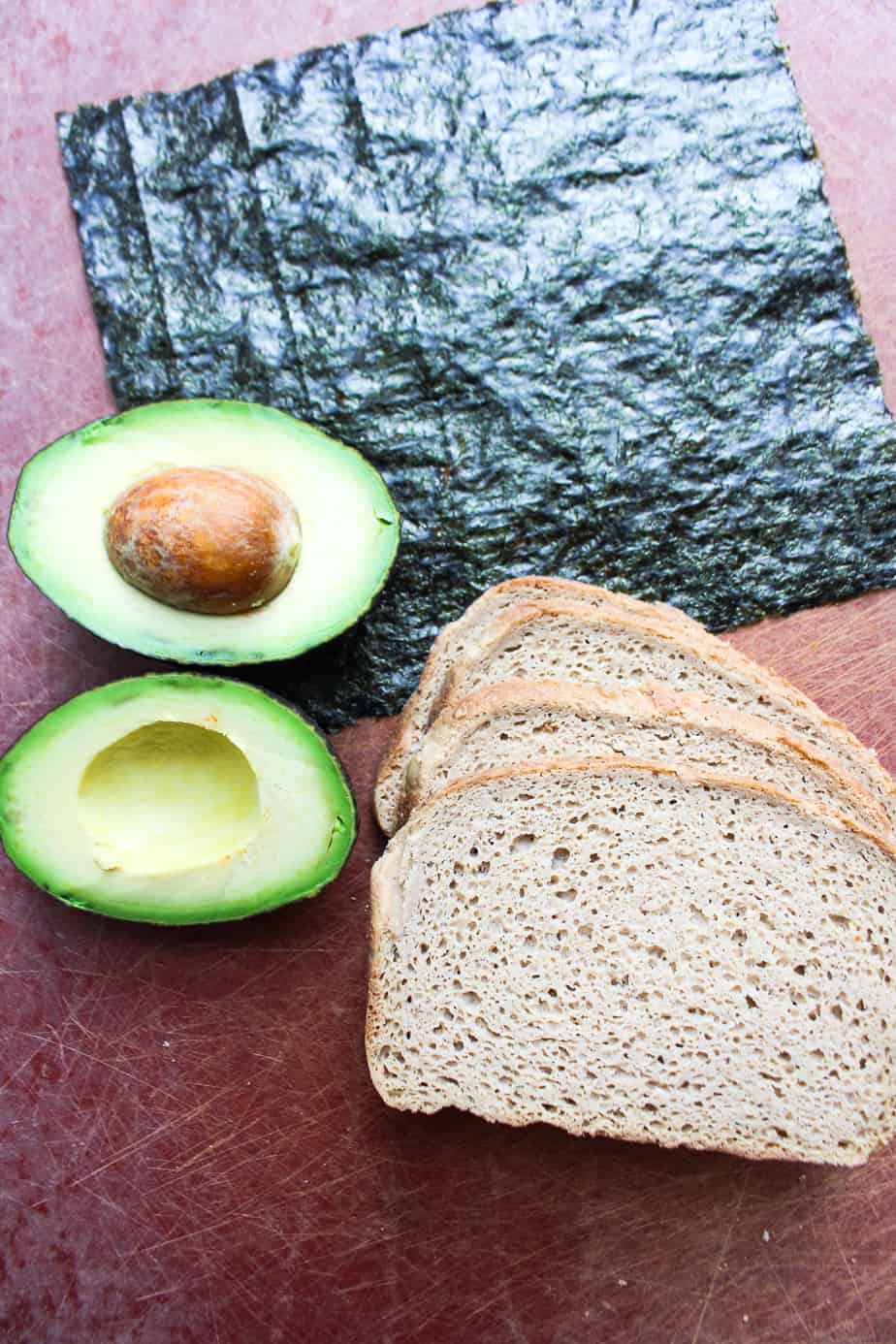 A sheet of nori, an avocado, cut open, and a stack of sliced bread