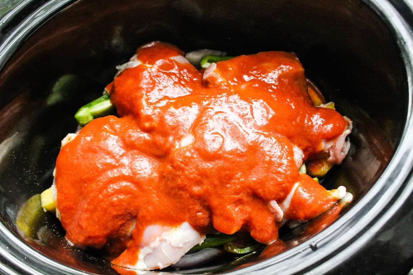 Slow cooker with pineapple, vegetables, white beans, and chicken thighs, topped with BBQ sauce