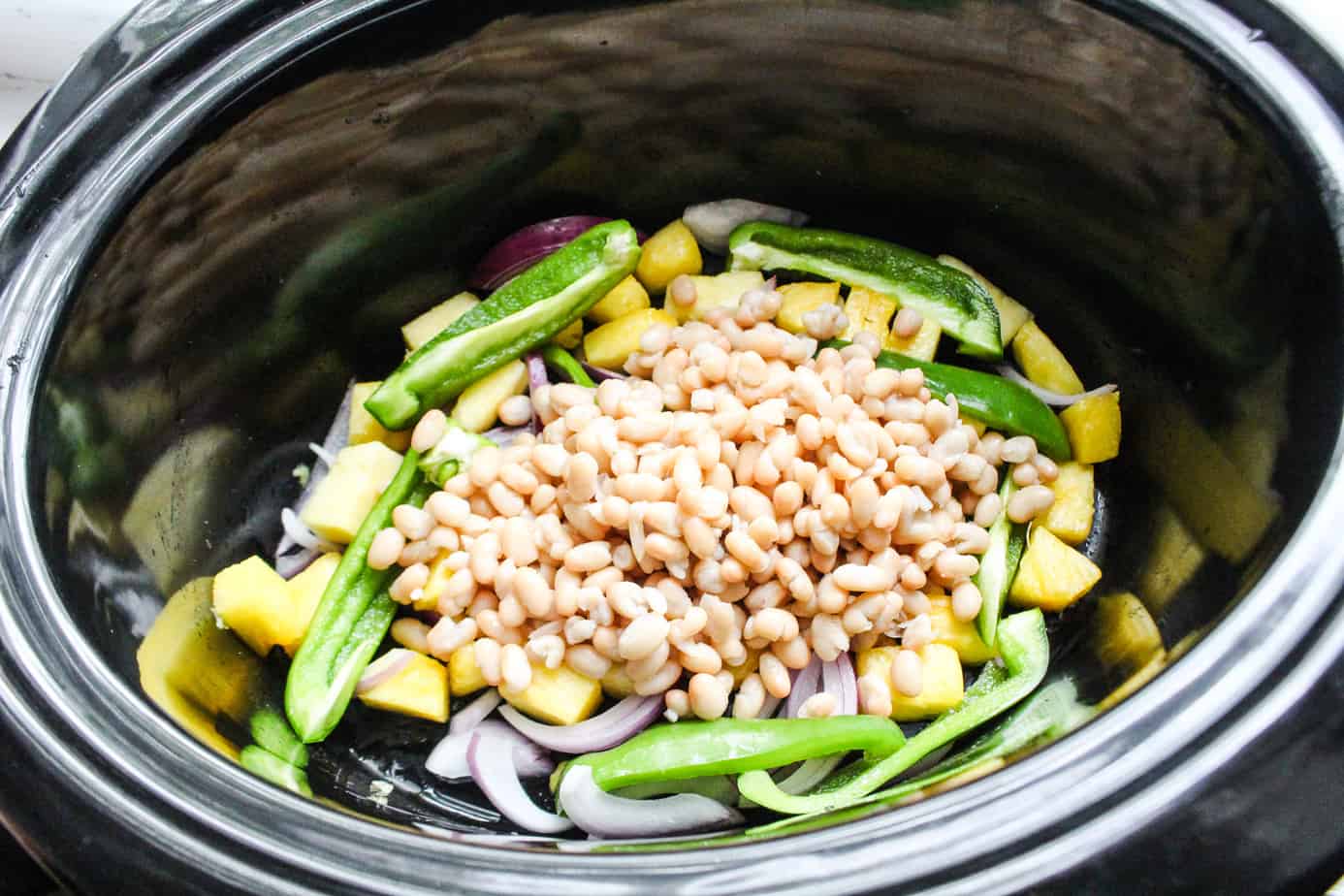 Large slow cooker with pineapple, sliced red onion, sliced green bell pepper, and white beans