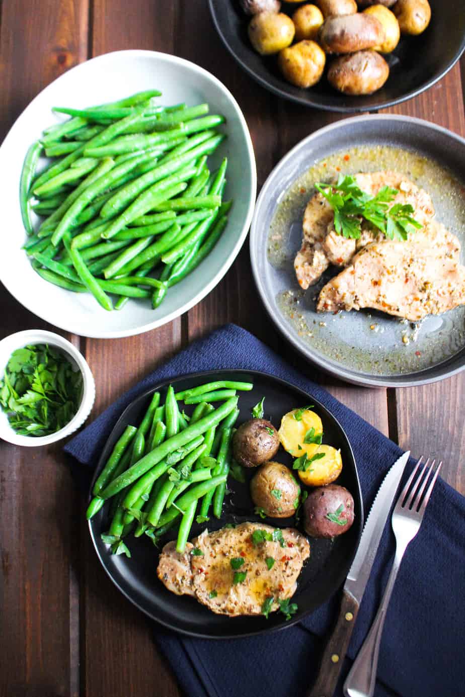 Crockpot pork chops on black plate with baby potatoes and steamed green beans.